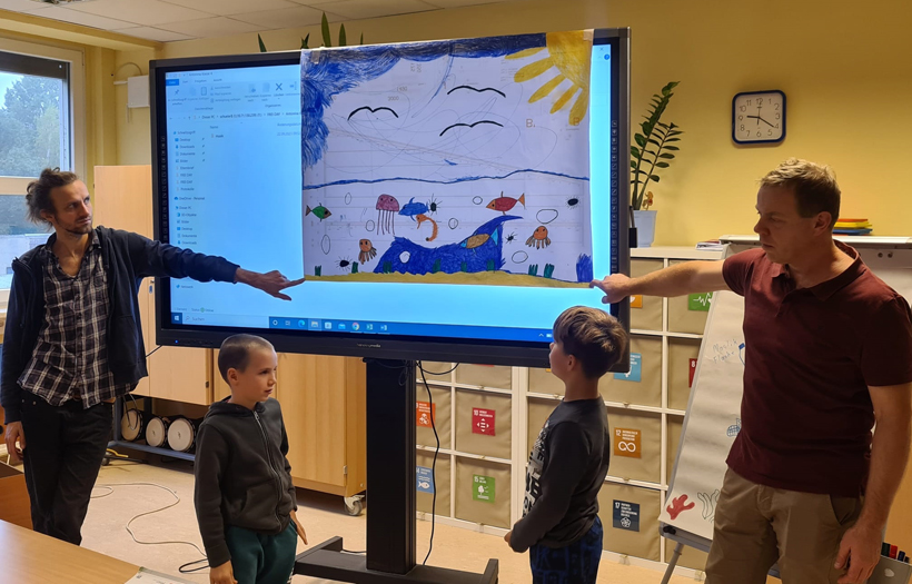 zwei Kinder und zwei Pädagogen vor der digitalen Tafel