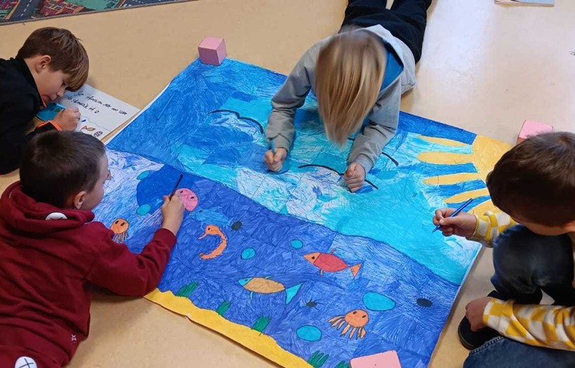 Vier Kinder malen auf dem Boden liegend ein Plakat