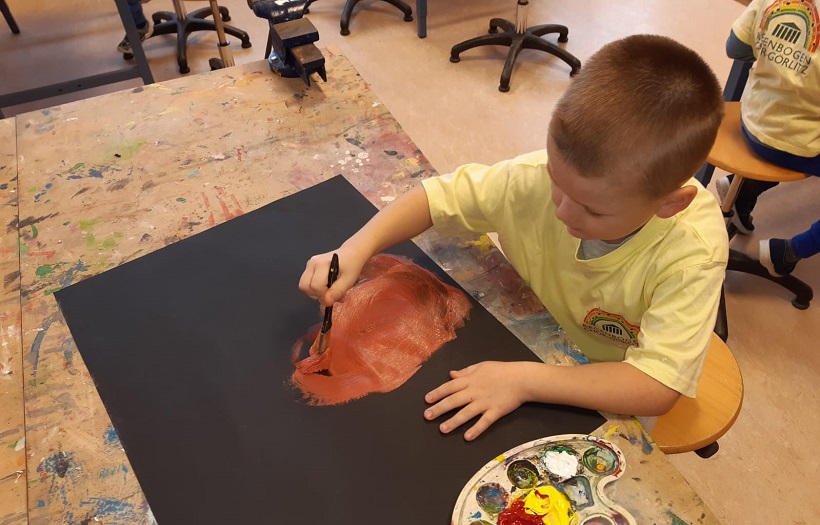 Vorschulkind malt Flammen auf A2 Papier mit Pinsel und Farbe zum Thema Die vier Elemente