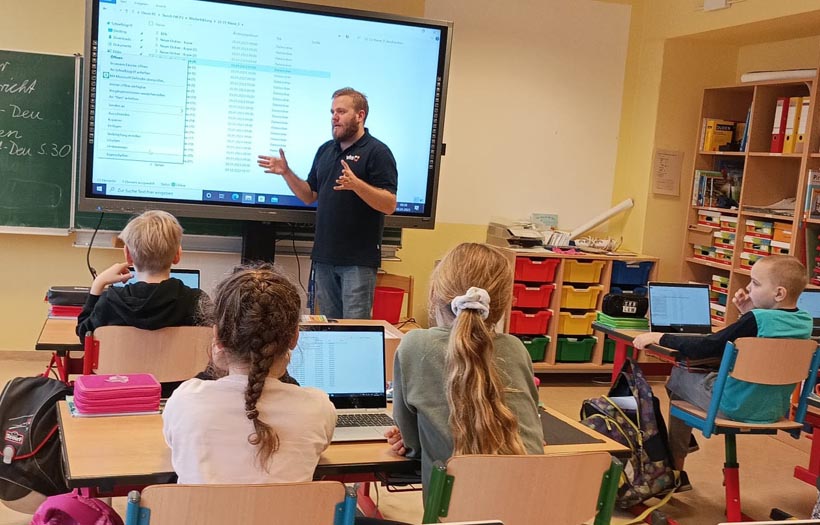 Schulklasse vor digitaler Tafel mit Notebooks auf den Tischen