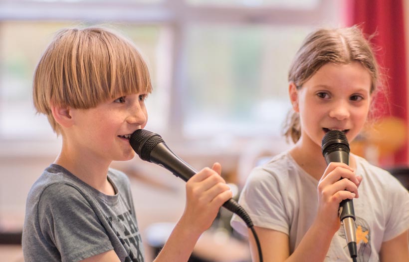 Ein Junge und ein Mädchen singen in Mikrofone