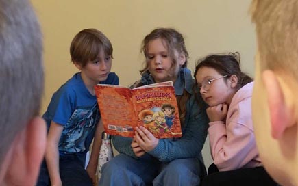 Mädchen sitzt zwischen zwei Kindern und liest vor